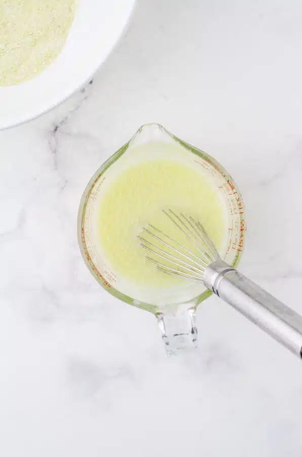 The wet ingredients for this cornbread recipe in a large measuring cup with a whisk in it.