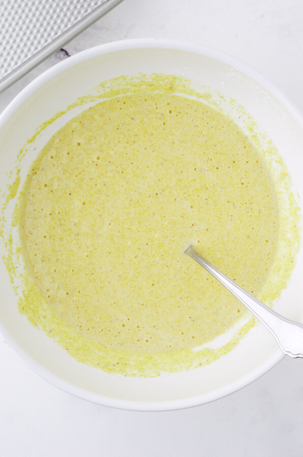 The cornbread batter in a large white mixing bowl with a mixing spoon in it.