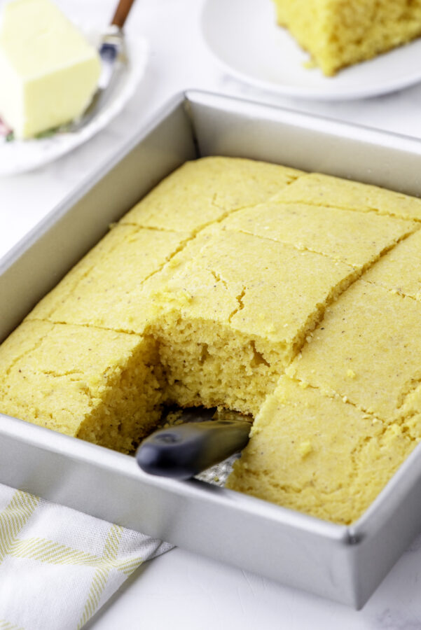A pan of baked cornbread with a slice taken out of it.