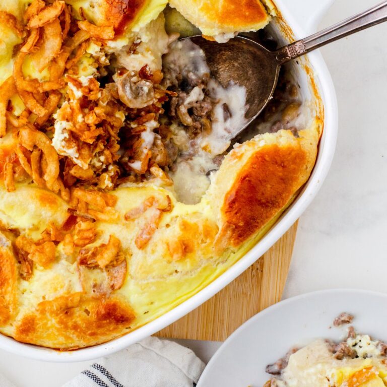 Stroganaff hamburger casserole with canned biscuits on top in a casserole dish with a serving spoon in it.