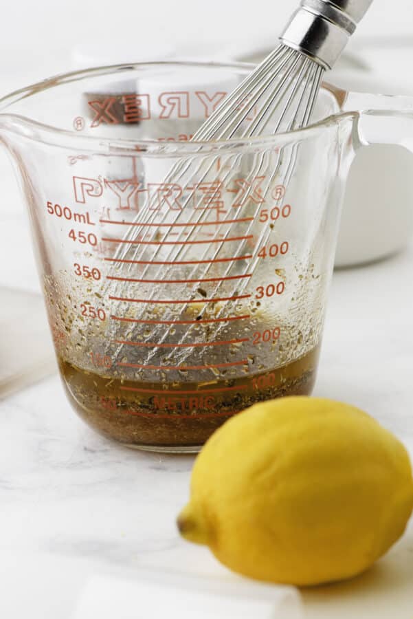 A whisk in the container of greek chicken marinade.