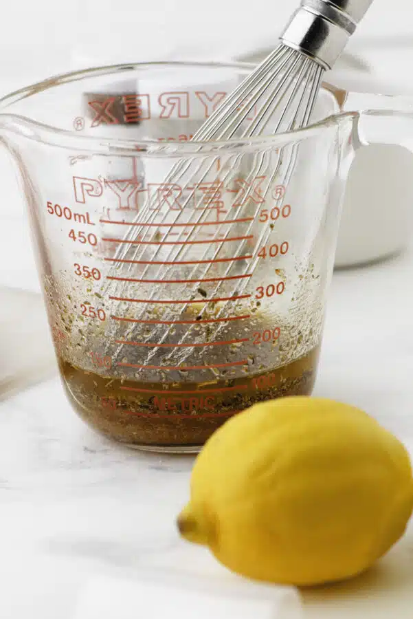 A whisk in the container of greek chicken marinade.