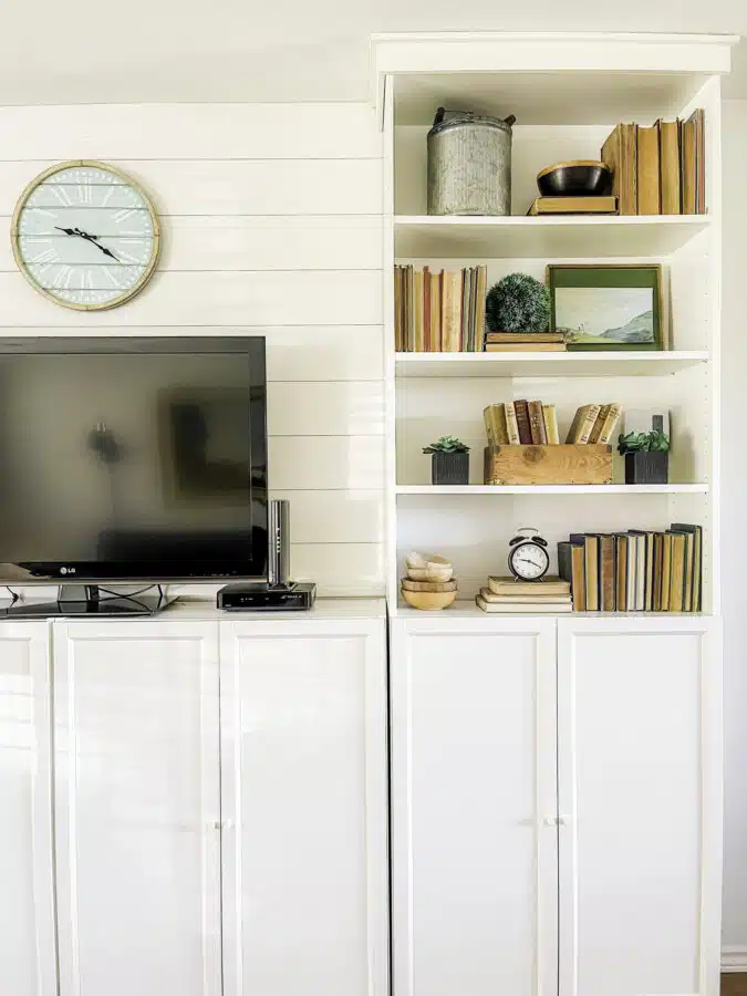 Living Room bookcase decorated with vintage books, wooden boxes, and greenery for an English Cottage look.