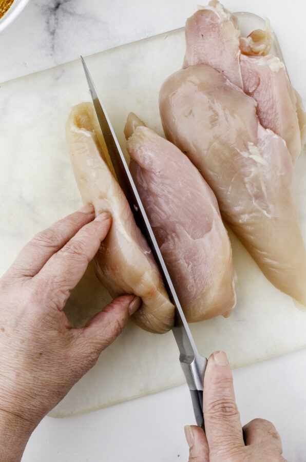 Slicing a chicken breast in half to make it thinner in preparation for chicken breast mexican marinade.