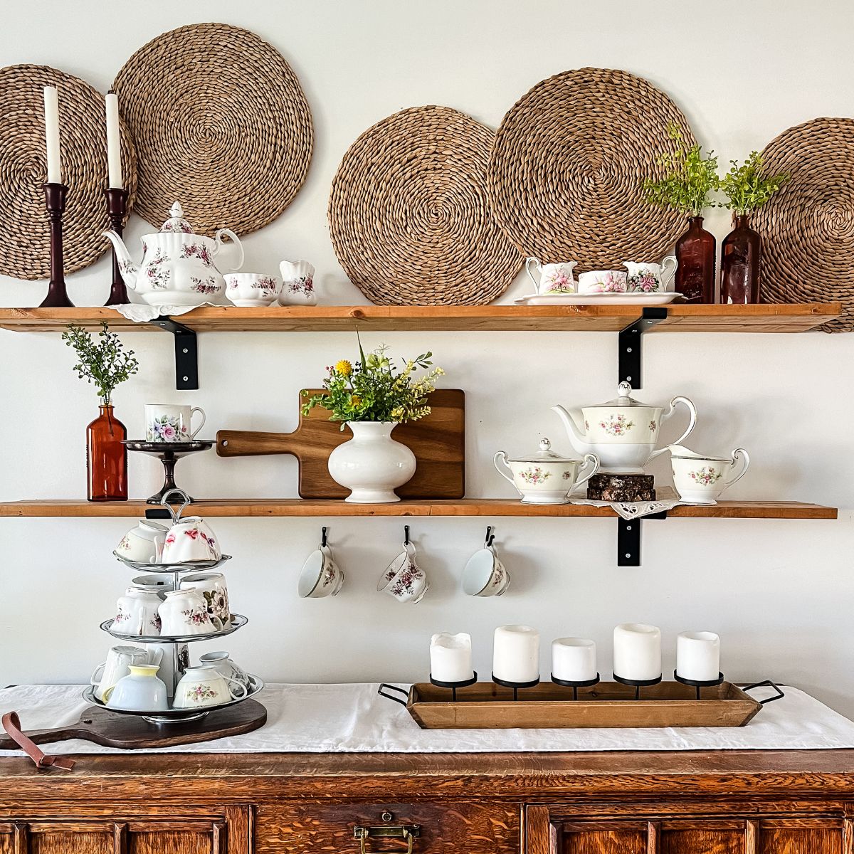 Shelves above a dining room hutch decorated with teapots, teacups, and greenery.