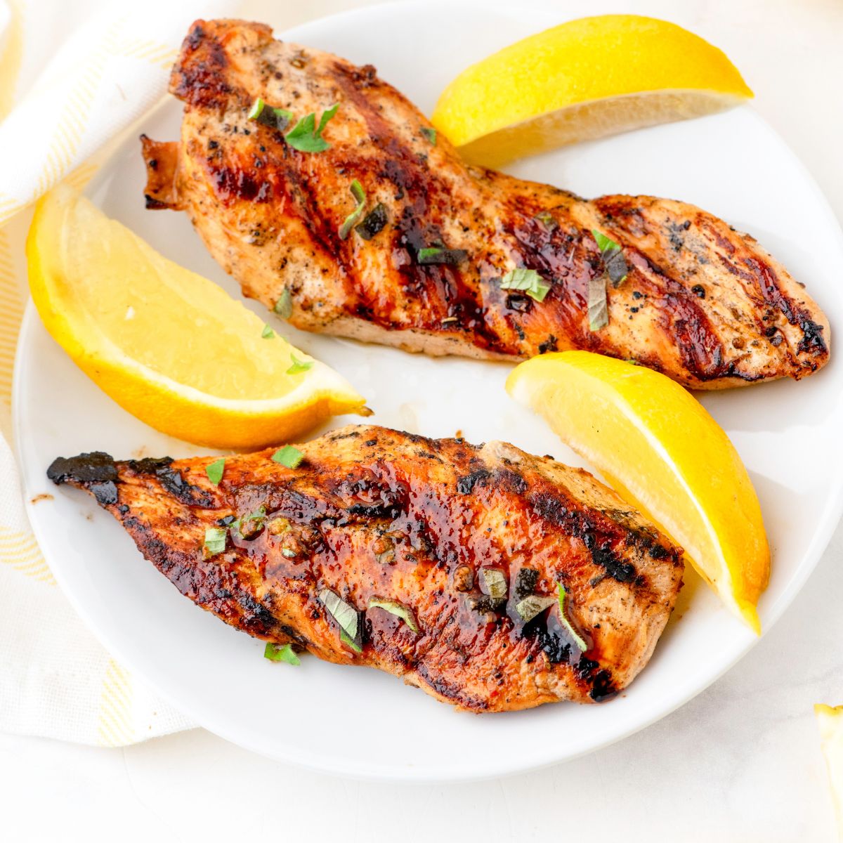 Plate of marinaded greek chicken that has been cooked on the grill with lemon slices around it.