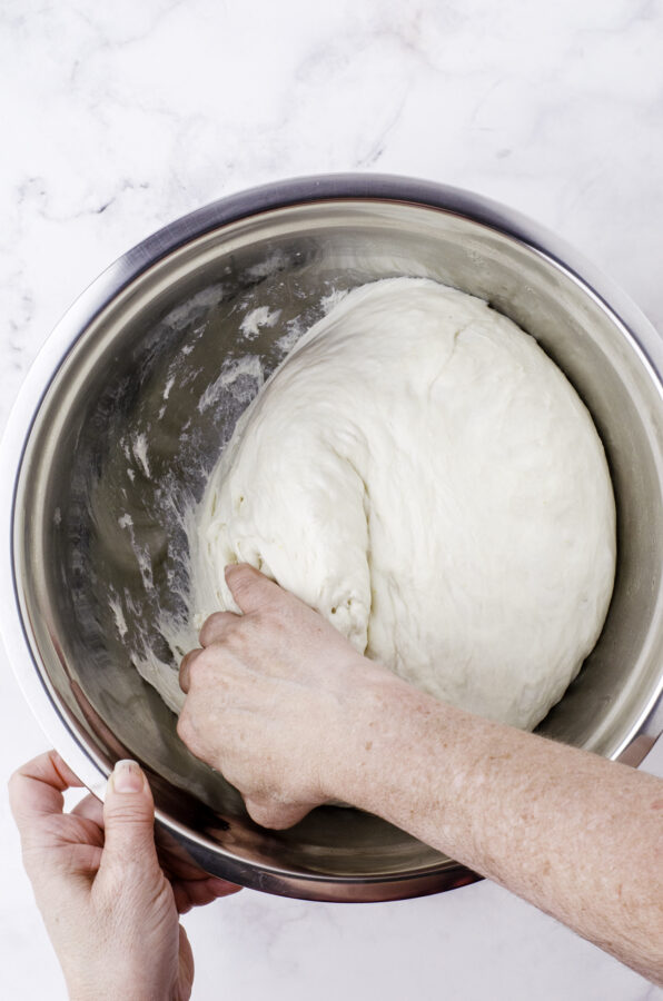 A woman pulling the sourdough dough away from the sides of the bowl.