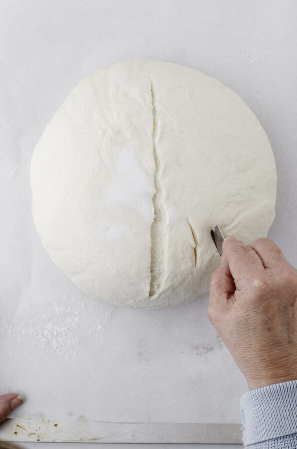 A woman using a straight razor blade to cut a pattern into the top of a sour dough loaf.