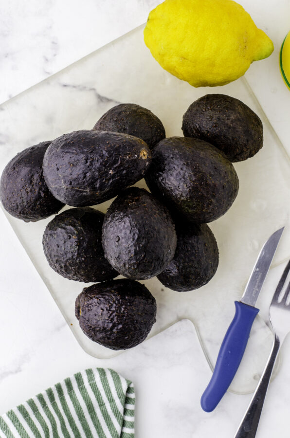 A pile of avocados and a lemon sitting on a cutting board.