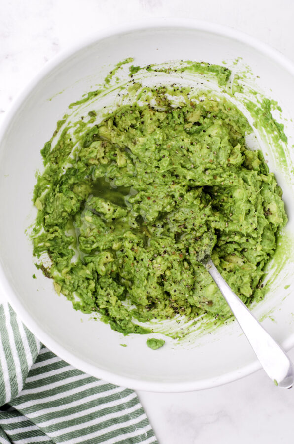 Avocados after they have been mashed with a fork in a large bowl.