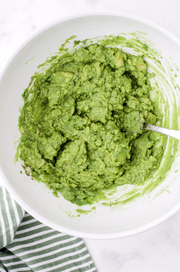 Mashed avocados with lemon juice and spices stirred together in a large bowl.