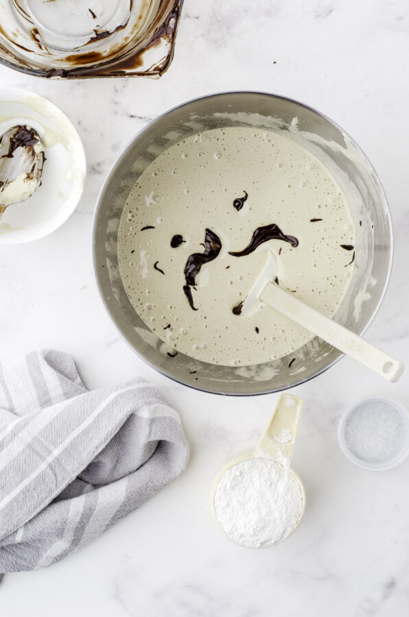 Smooth melted chocolate being added to the bowl of beaten eggs and sugar.