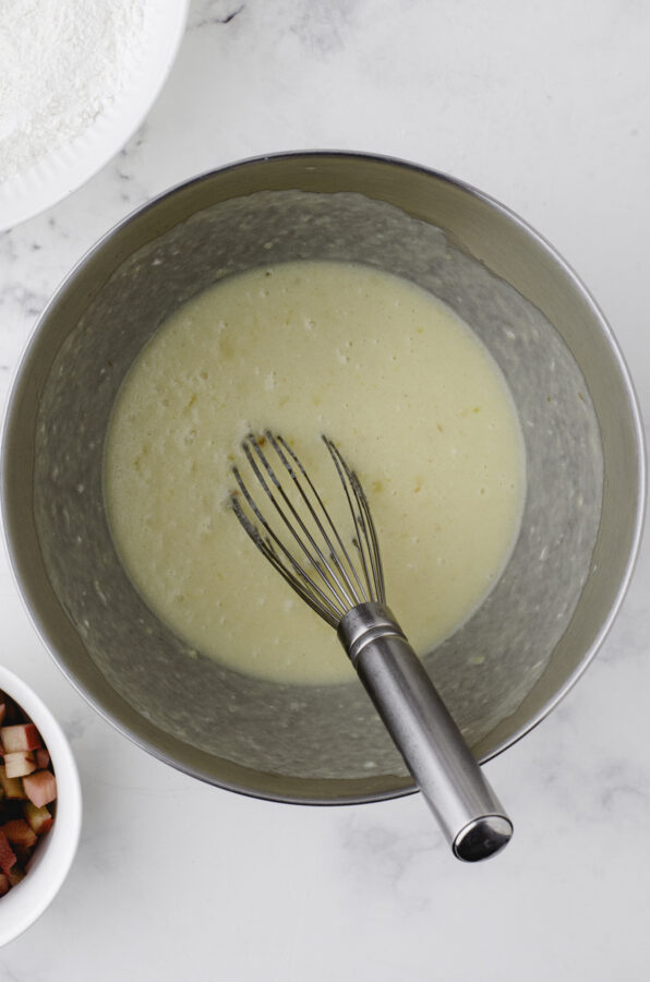 Wet ingredients and brown sugar stirred with a whisk in a large mixing bowl for sourdough rhubarb muffins recipe.