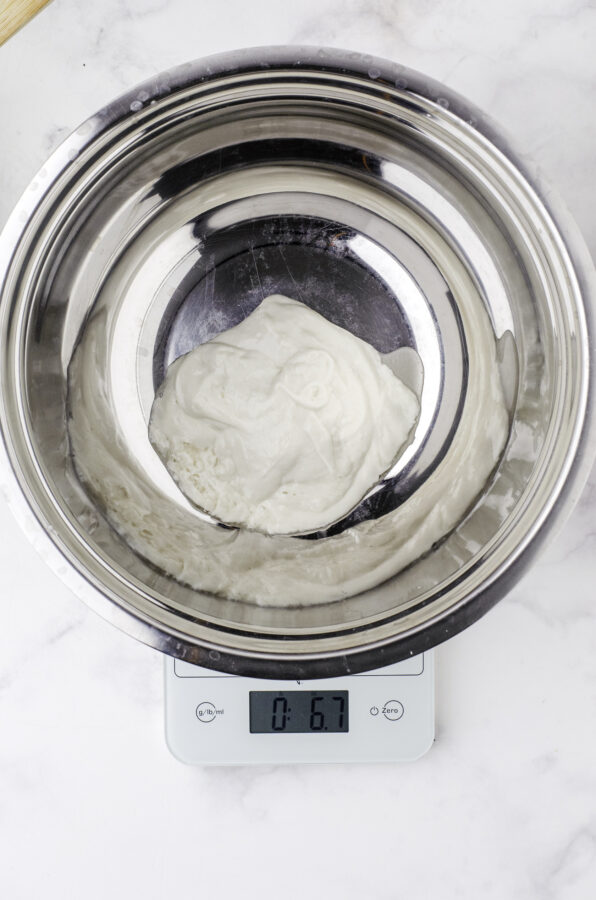 Sourdough starter in a metal bowl being weighed on a kitchen scale. Step 1 of feeding sourdough starter.