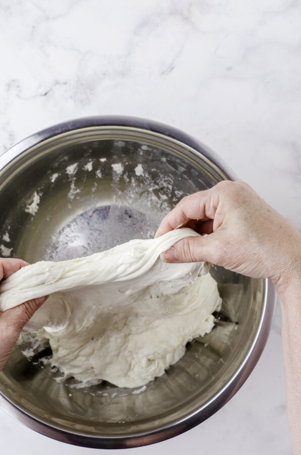 Stretching sour dough bread by pulling up on one side of the dough and holding it in two hands.