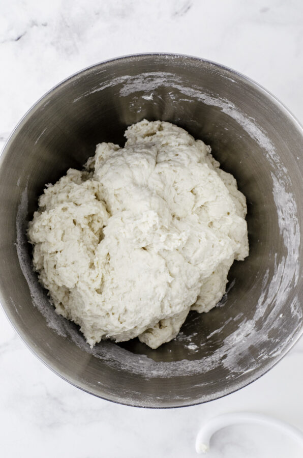 Sourdough bread dough in the mixing bowl of a stand mixer after the flour has been added in and mixed with a dough hook. It isn't super smooth.