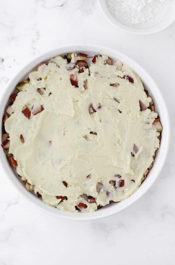 The cake batter smooth on top of diced rhubarb in a round white baking dish.