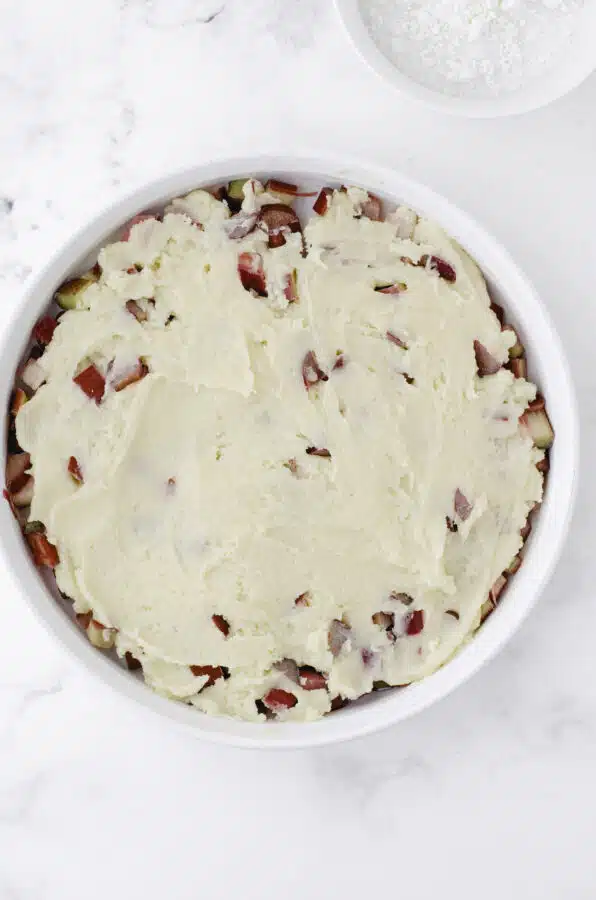 The cake batter smooth on top of diced rhubarb in a round white baking dish.