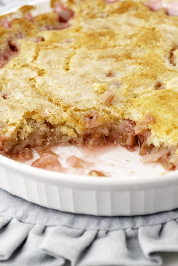 A pan of rhubarb pudding cake that has had one serving taken out of it so you can see how juicy the inside is.
