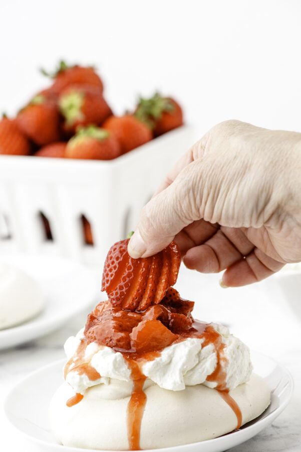 A strawberry being placed on the top of a strawberry pavlova dessert.