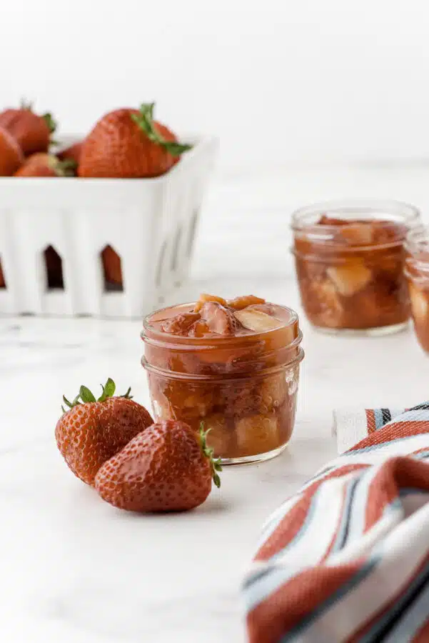 Strawberry sauce in a small mason jam jar with a basket of fresh strawberries behind.
