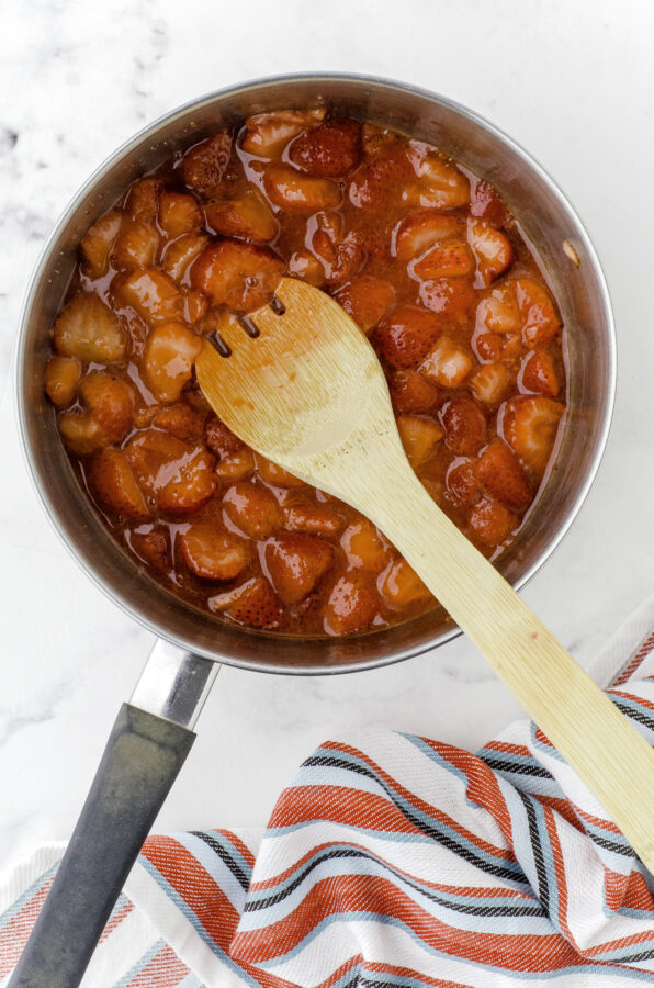 Strawberry sauce in a medium saucepan after it has been cooked, with a wooden spoon in it.