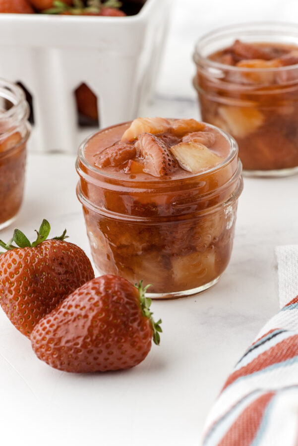 A jar of strawberry sauce with 2 other jars of sauce in the background.