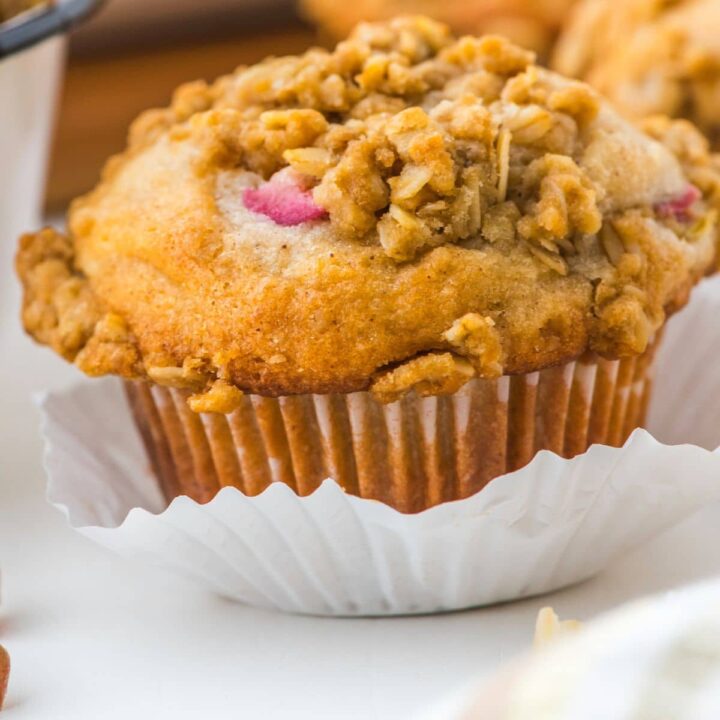 A sourdough discard rhubarb muffin with oat crumble topping on a white paper muffin cup liner