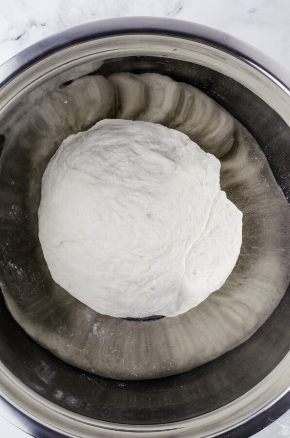 Sourdough bread dough after it has been kneaded slightly and formed into a ball and placed in a large metal bowl to proof.