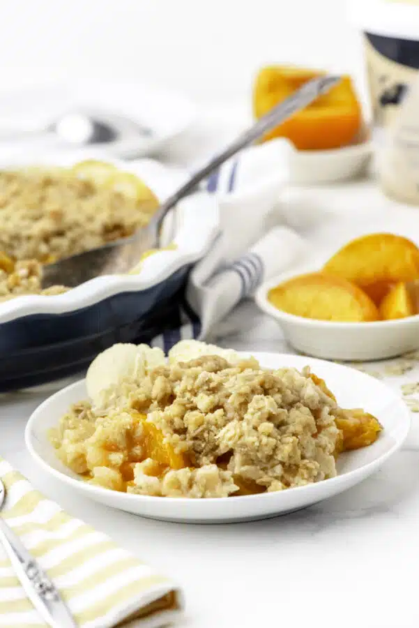 Peach crisp with ice cream on a dessert plate.