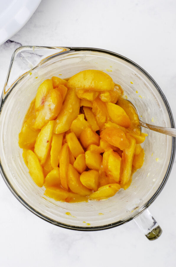 A bowl of sliced peaches with flour and sugar stirred into it.