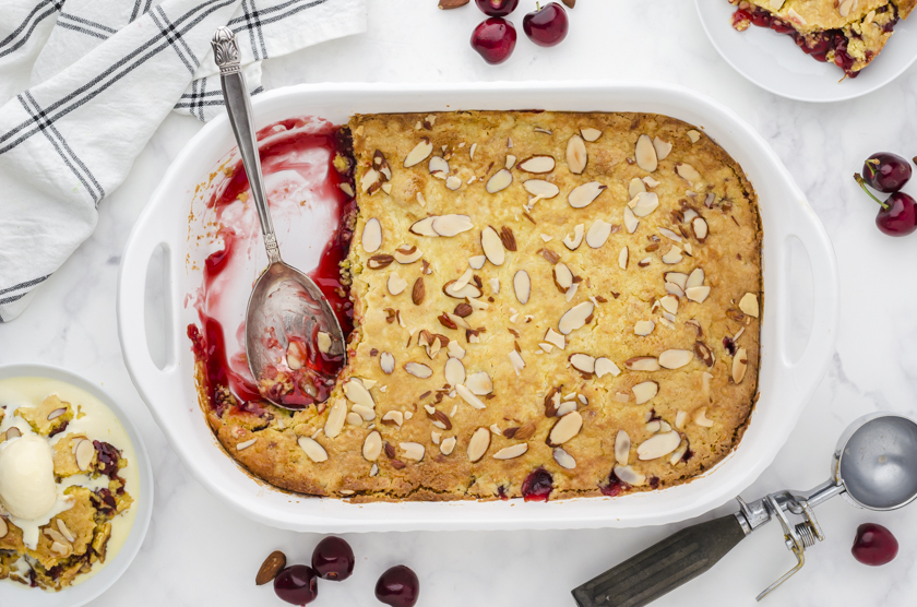 A pan of cherry dump cake with a few pieces dished out onto serving plates.