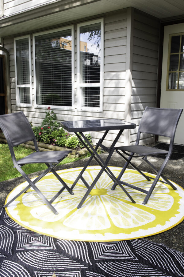 A 3 piece bistro table set sitting on a round outdoor rug.