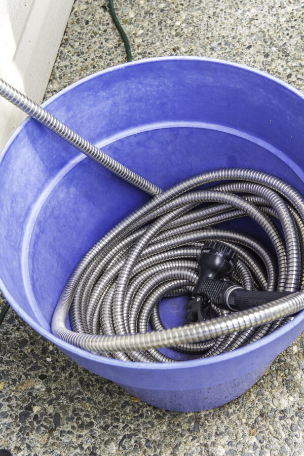 A metal garden hose wound up in a large plastic planter.