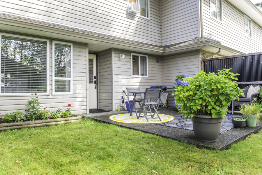 A small concrete slap patio outside a townhouse with a flower bed on one side.