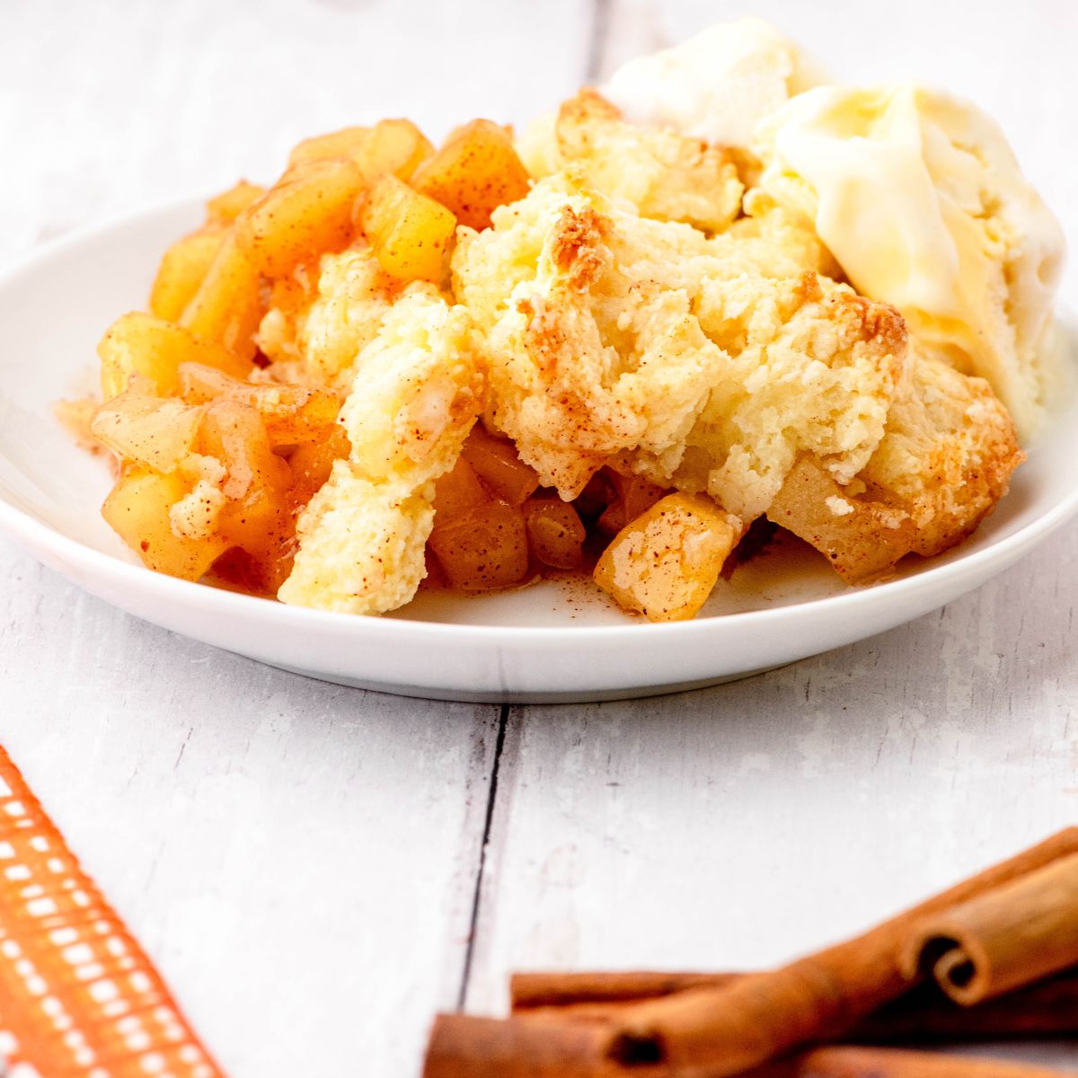 A dessert plate with a serving of apple cobbler on it topped with a scoop of vanilla ice cream.