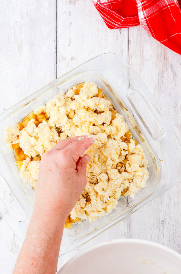 Apple cobbler topping being put on hot apple pie filling in a square 8x8 inch baking dish.