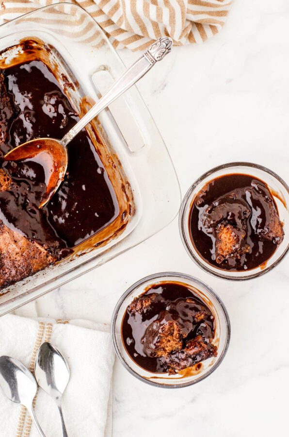 A pan of chocolate pudding cake with two dessert bowls with servings of the cake in them.