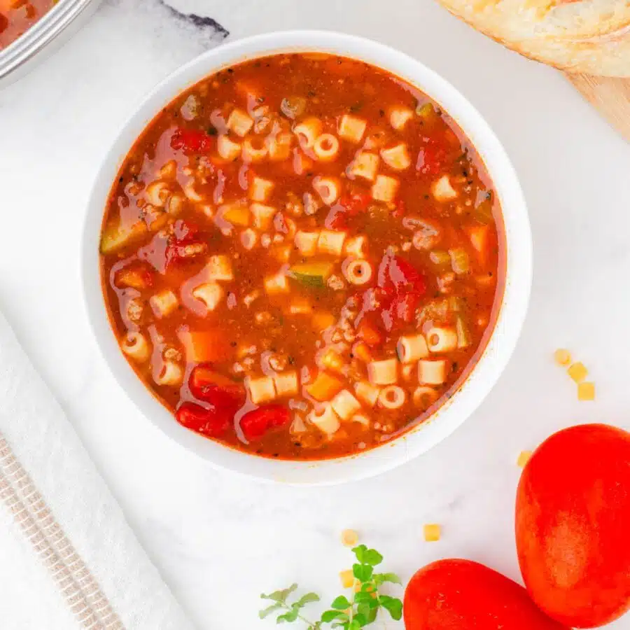 A bowl of minestrone soup with fresh tomatoes beside it.