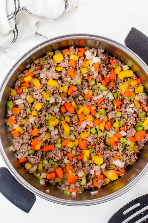 A large stock pot with browned ground beef and veggies as the base for minestrone soup.