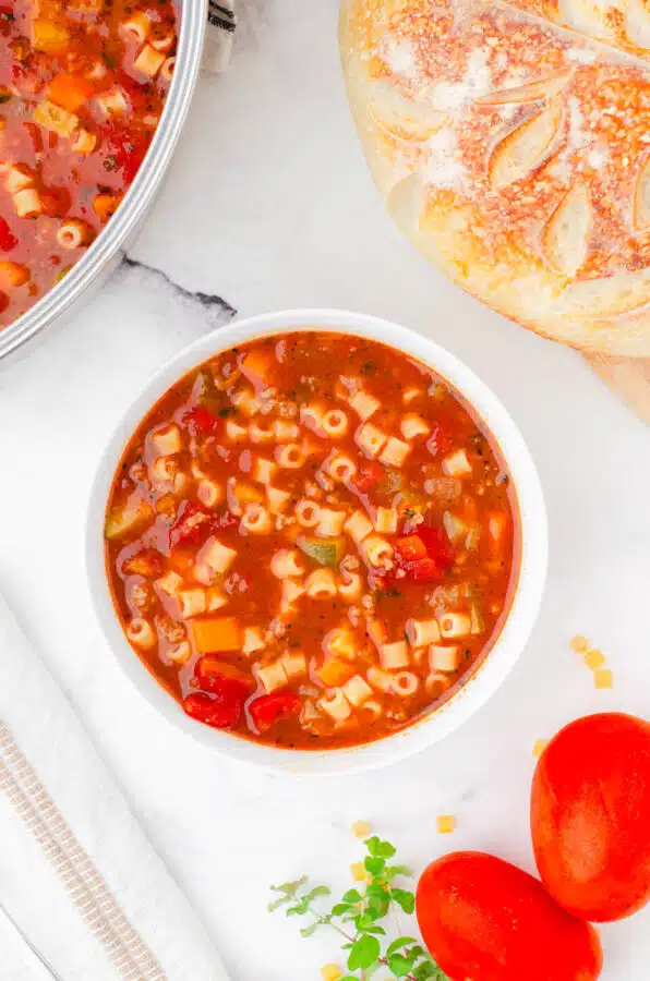 A bowl of minestrone soup with a large pot of minestrone soup beside it.