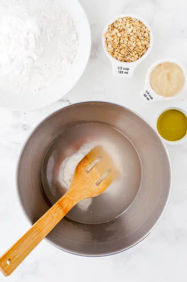 Water, sourdough starter, and salt in the bowl of an electric mixer ready to be stirred.