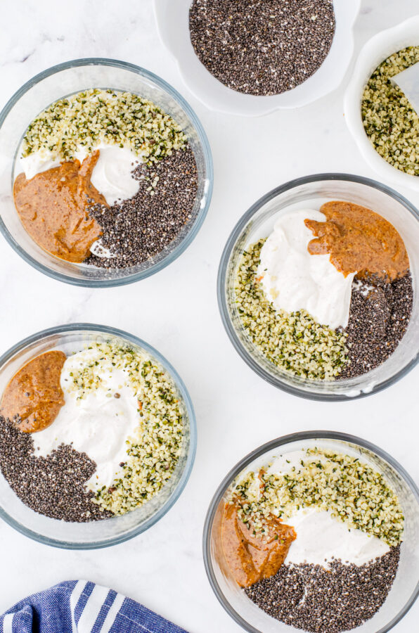 4 clear glass bowls with greek yogurt, almond butter, chia seeds, and hemp seeds in each one.