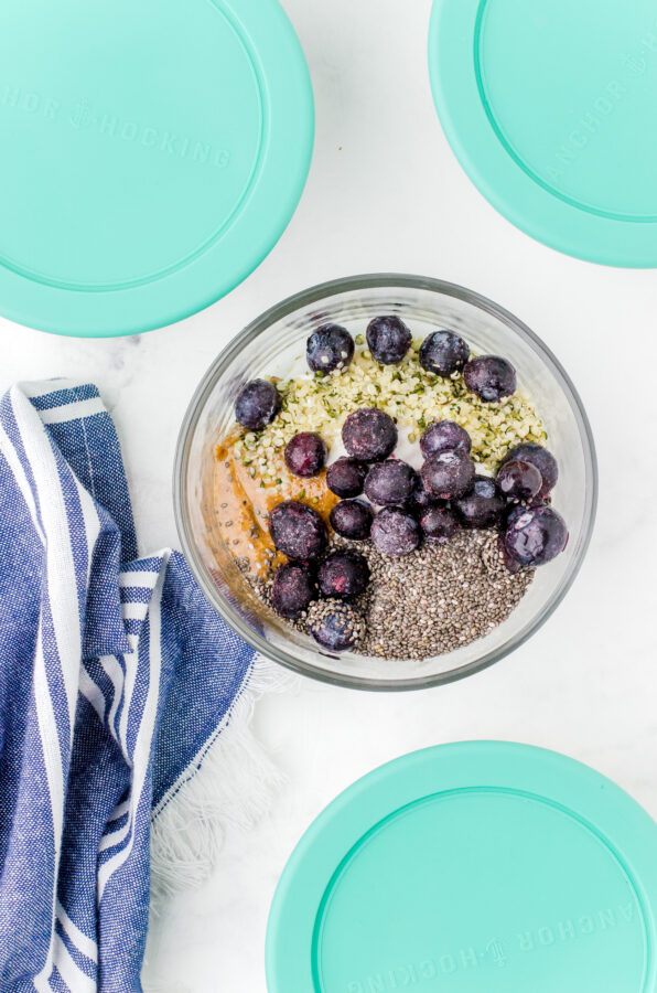 a yogurt bowl assembled with berries on the top and other yogurt bowls with lids surrounding it.