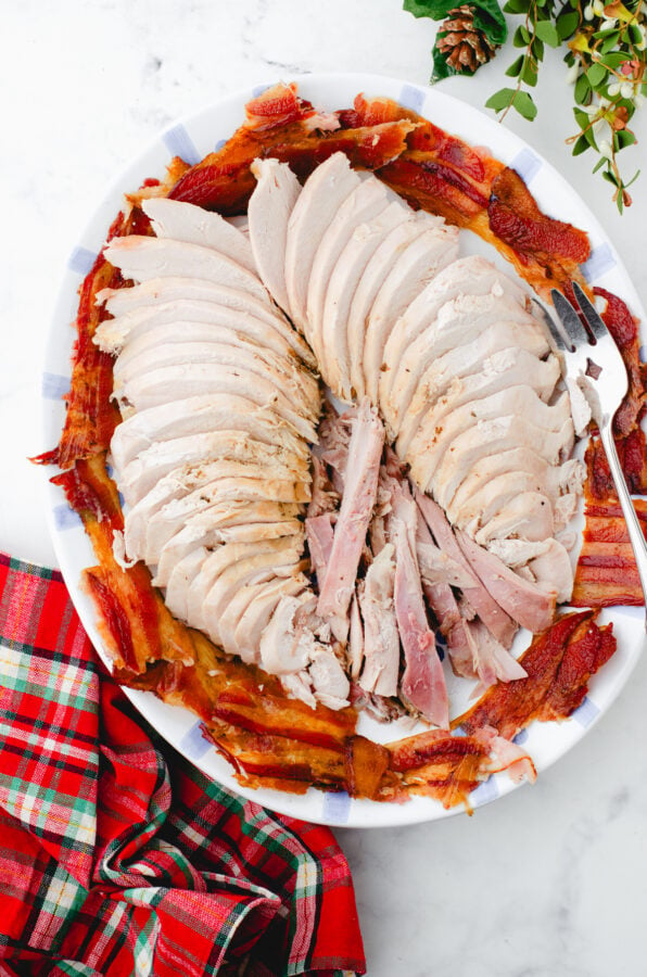Roast turkey sliced on a plate with bacon around it