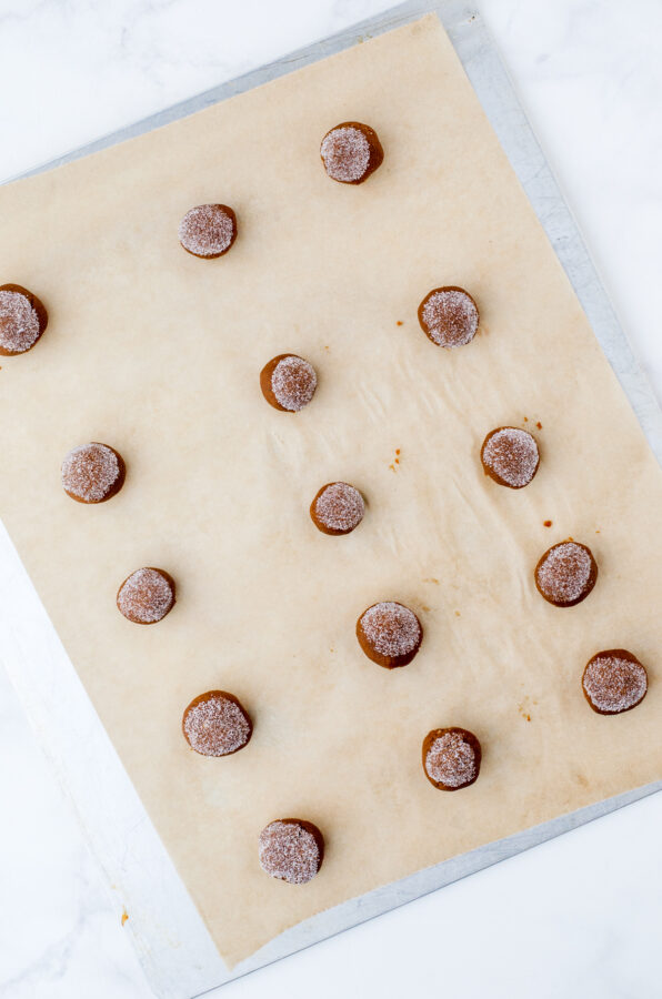 Gingersnap cookie dough in balls dipped in sugar on a baking sheet ready to be put in the oven.