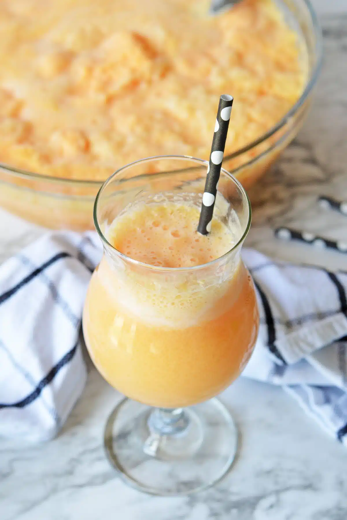 Glass of orange sherbet punch beside a punch bowl