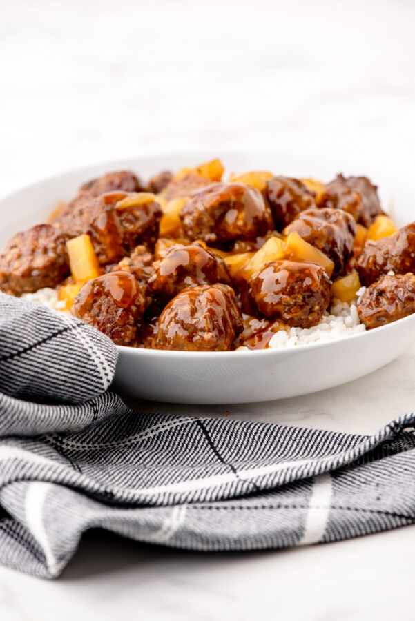 Bowl of sweet and sour meatballs with pineapple tidbits over a bed of rice.