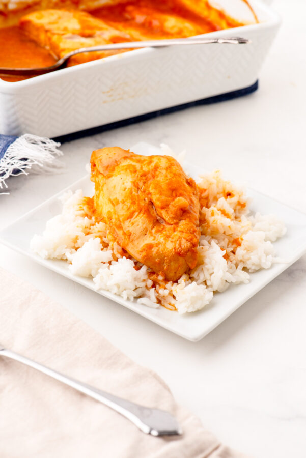 A piece of apricot chicken on a bed of rice on a white plate.