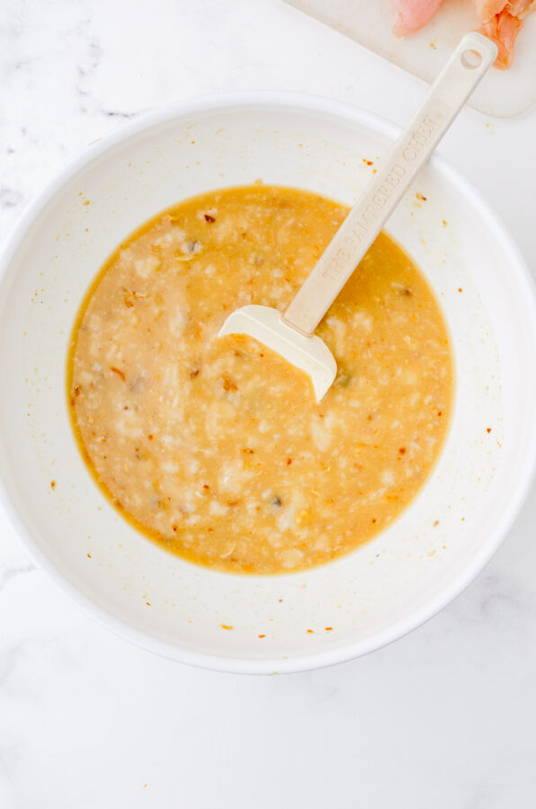 Rice, chicken broth, onion soup mix, and mushroom soup being mixed in a bowl for chicken rice pilaf.